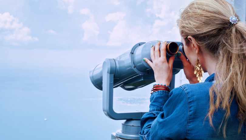 woman in blue denim jacket holding a gray steel tower viewer